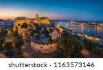 Budapest, Hungary - Aerial panoramic skyline view of beautiful illuminated Buda Castle Royal Palace with Szechenyi Chain Bridge, Hungarian Parliament at blue hour