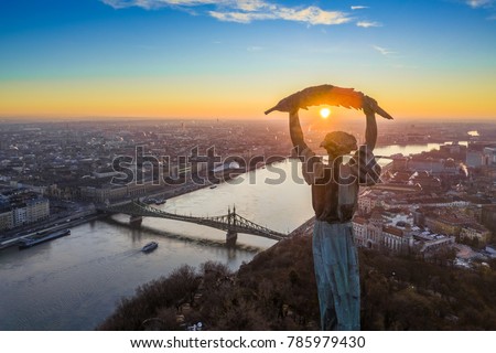 Budapest, Hungary - Aerial panoramic sunrise view at the Statue of Liberty with Liberty Bridge and sightseeing boat on River Danube taken from Gellert Hill