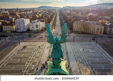 Budapest, Hungary - Angel sculpture from behind on the top of Heroes' Square at sunset with Andrassy street and the skyline of Budapest at background
