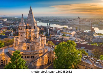 Budapest, Hungary - Beautiful golden summer sunrise with the tower of Fisherman's Bastion and green trees. Parliament of Hungary and River Danube at background. Blue sky. - Shutterstock ID 1560652652
