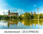 Budapest, Hungary - June 19, 2024: Vajdahunyad Castle (copy of Hunyad Corvin Castle) during golden hour time. Moving catamarans in the pond on the foreground. Sunny summer day, clear sky.