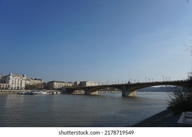Budapest, Hungary - March 24th 2022 : 
View Of The Margaret Bridge And The Danube River And The Hungarian Parliament Building From A Distance And The People At The Bridge At The Blue Clear Sky Day