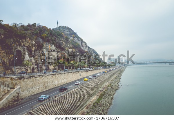 Budapest, Hungary - Nov 6, 2019: Gellert Hill\
Cave Church, Sziklatemplom. Liberty Statue on the top of the hill.\
Cars on the road in front of the hill by the Danube river.\
Hungarian landmarks.