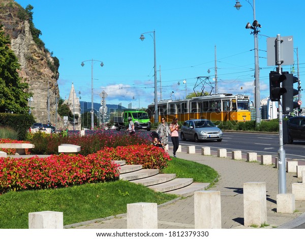 Budapest, Hungary - September 02, 2020: Gellért\
Square traffic with cars and yellow tram at the flowery foot of the\
Gellért hill