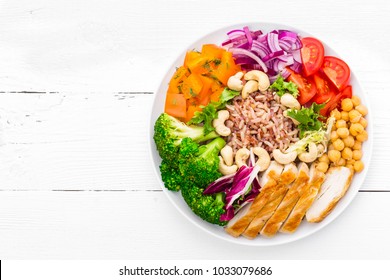 Buddha bowl dish with chicken fillet, brown rice, pepper, tomato, broccoli, onion, chickpea, fresh lettuce salad, cashew and walnuts. Healthy balanced eating. Top view. White background