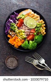 Buddha bowl dish with chicken fillet, brown rice, avocado, pepper, tomato, broccoli, red cabbage, chickpea, fresh lettuce salad, pine nuts and walnuts. Healthy balanced eating. Top view