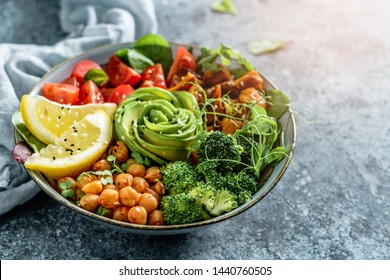 Buddha-Schüssel Salat mit gebackenen Süßkartoffeln, Kichererbsen, Brokkoli, Tomaten, Grün, Avocado, Erdnüsse auf hellblauem Hintergrund mit Serviette. Gesunde veganische Lebensmittel, sauberes Essen, Diät, Nahaufnahme