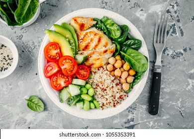Buddha bowl with spinach salad, quinoa, roasted chickpeas, grilled chicken, avocado, tomatoes, cucumbers, sesame seeds. Top view