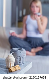 Buddha Candles With Palo Santo Sticks And A Blonde Woman In A Meditation Pose In The Background.