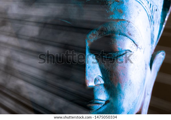 Buddha face close-up. Spiritual\
enlightenment. Zen Buddhism. Traditional Thai statue with ethereal\
light. Peaceful blue tone meditation image. Awakening the mind of\
self with Buddhist\
mindfulness.