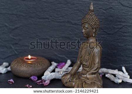 Buddha figure with a candle in front of a dark background.