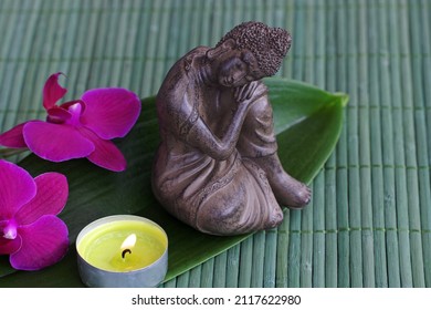 Buddha figure with orchid flower and scented candle on a bamboo mat.