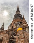 Buddha statue in golden robe against the backdrop of a central Chedi in Wat Yai Chai Mongkol in Ayutthaya, Thailand. Monastery of Auspicious Victory against cloudy sky background