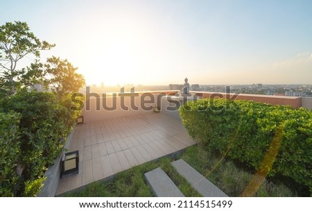 A buddha statue on sky garden on private rooftop of condominium or hotel, high rise architecture building with tree, grass field, and blue sky.