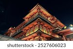 The Buddha Tooth Relic Temple shines brightly at night, highlighting its intricate architecture. The warm lights create a serene atmosphere in Singapore