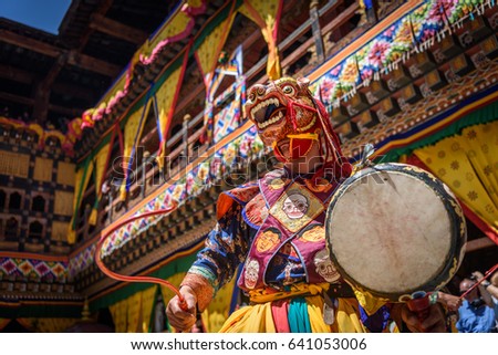 Buddhist Monk dancing and holding a drum at colourful mask dance at yearly buddhism Paro Tsechu festival in Bhutan monastery temple location.