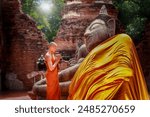 Buddhist monks dressed in orange robes walking at a temple grounds, He cover the Buddha with yellow robes as an offering of respect. Inside the ancient temple of Ayutthaya world Heritage site