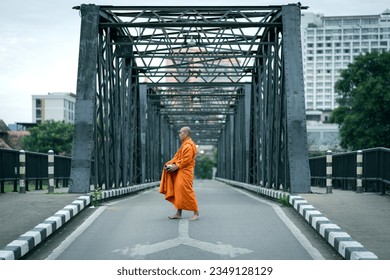 Buddhist monks are morning walking on routes between rural villages on the ancient iron bridge the travel destination of Chiang Mai, Thailand. Concepts make merit with monks in culture and religion.