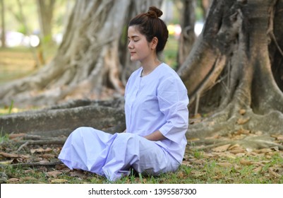 Buddhist Nun woman or woman priest  or hindu nun smiling in white dress try to practice meditation and siting under the tree in the garden  - Powered by Shutterstock