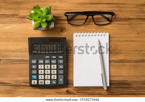 Budget for the next year concept.\
Flat lay above overhead close up view photo of blank notebook\
eyeglasses calculator flower isolated light color brown\
backdrop