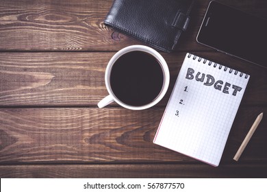 Budget planing concept. Top view of notepad with word Budget, mobile phone, cup of coffee, pouch on wooden background. Write idea success solution concept. Vintage toned picture. Copy space