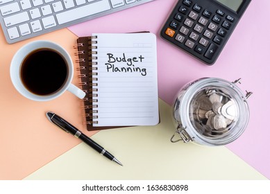 Budget Planning text on note pad with cup of coffee, calculator, computer keyboard, coin jar and pen on colorful pastel colored background