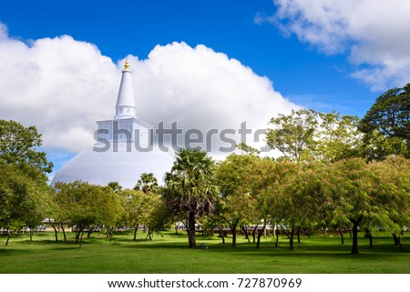 Budhist stupa Ruwanweliseya in Anuradhapura, Sri Lanka. White stupa with golden top in background with green park palm tree and grass field in foreground. Stupa Ruwanweliseya, Anuradhapura, Sri Lanka