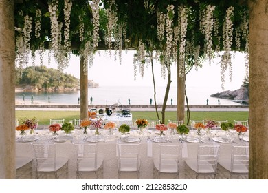 Budva, Montenegro - 15.07.21: Wedding dinner table reception. A very long table for guests with a white tablecloth, floral arrangements, glass plastic transparent chairs Chiavari