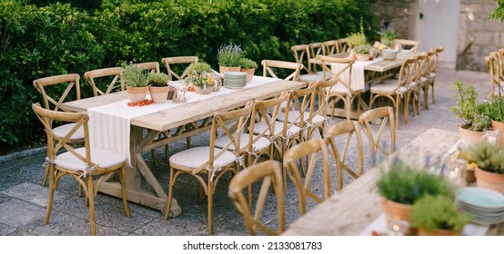Budva, Montenegro - 17.07.21: Wedding dinner table reception at sunset outside. Ancient rectangular wooden tables with rag runner, wooden vintage chairs, lavender pots