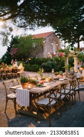 Budva, Montenegro - 17.07.21: A wooden table for guests at the wedding, decorated with a raner and clay pots with lavender. Artificial lighting of the open-air banquet hall. 