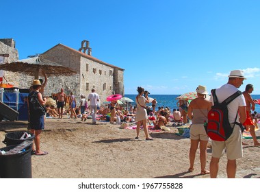 Budva, Montenegro, Adriatic Sea  - 08.23.2014: People On A Public Beach By The Wall Of Old Town Budva. Overcrowded Beach. Sunbathing Tourists. Mediterranean Holidays.