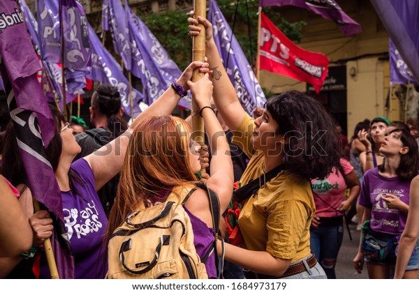 Buenos Aires, Argentina, 09/03/2020:  Women\
helping each other holding a sign in the protest on a windy day.\
Sorority and companionship concept. International Women\'s day\
strike for equal rights.