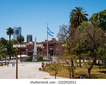 Buenos Aires, Argentina -10 7 2022: The Flag Of Argentina Flies Above The City Square Gardens And Government Offices In Plaza De Mayo, Buenos Aires. Plain Blue Sky. Space For Text. 