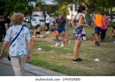 BUENOS AIRES, ARGENTINA - Mar 10, 2021: Selected Focus Of Lady Walking Through A Park And Looking At A Group Of People Exercising Outdoors During The New Normal