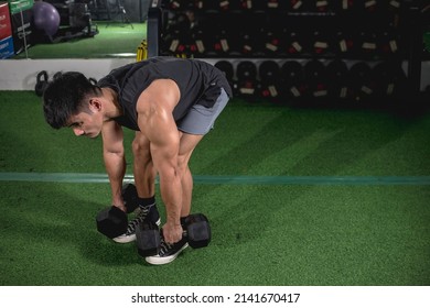 A buff and muscled asian man picks up a pair of dumbbells for a set of bent-over rows. Weight and resistance training at the gym. - Powered by Shutterstock