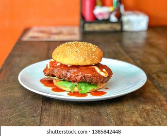 Buffalo burger chicken sandwich topped with tomato lettuce homemade buffalo wings sauce and mayonnaise on toasted sesame seed burger bun cooked and deep fried to perfection sitting in white plate