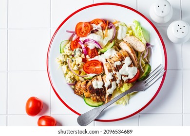 Buffalo chicken salad with gorgonzola cheese, tomato, cucumber and ranch dressing, white tile background, top view. - Shutterstock ID 2096534689