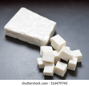 Buffalo Paneer Indian Cheese On Black Slate Cutting Chopping Board Counter In One Large Piece And Smaller Cubes 