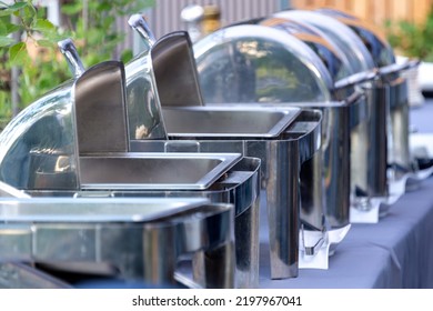 Buffet Heated Trays Standing In Line Ready For Service. Outdoors Buffet Restaurant, The Hotel Restaurant. Warming Trays For Buffet Line On The Table Outdoors