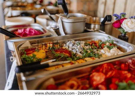 Buffet table with assorted cheeses, herbs, and fresh greens in a stainless steel tray, ready to serve at a catered event.