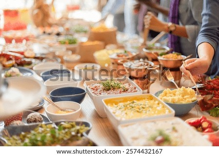 A buffet table with diverse dishes, including salads, sauces, and main courses. People serve themselves from the buffet, enjoying a variety of colorful foods. Buffet table with delicious food.