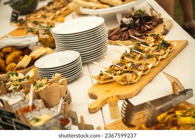 A buffet table at a party with a large amount of prepared food. A wooden tray with a salmon fish delicacy dominates.