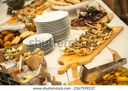 A buffet table at a party with a large amount of prepared food. A wooden tray with a salmon fish delicacy dominates.