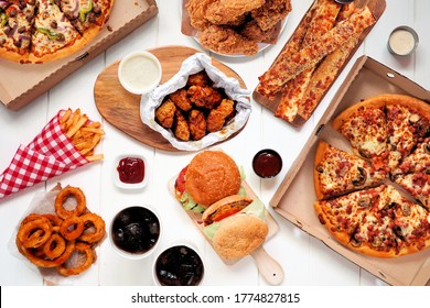 Buffet table scene of take out or delivery foods. Pizza, hamburgers, fried chicken and sides. Top view on a white wood background. - Shutterstock ID 1774827815