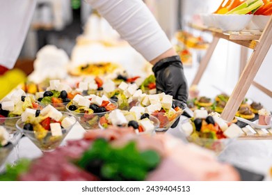 buffet where a person in gloves serves a variety of fresh salads. Colorful bowls contain ingredients like cheese cubes, olives, and chopped vegetables. - Powered by Shutterstock