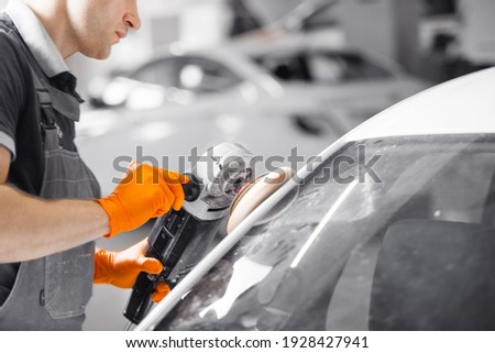 Buffing of white car, worker with polishing machine recovers bodywork. Automobile detailing.