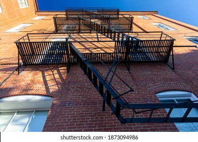 Bug eye view of vintage black metal construction fire escape ladder with makeshift balconies and access to egress windows attached on the side of an old  brick apartment. 