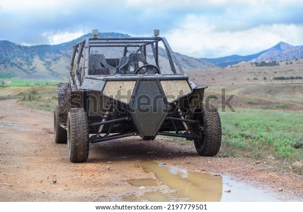 Buggy on a dirt road in the background of a mountain\
landscape in the rain