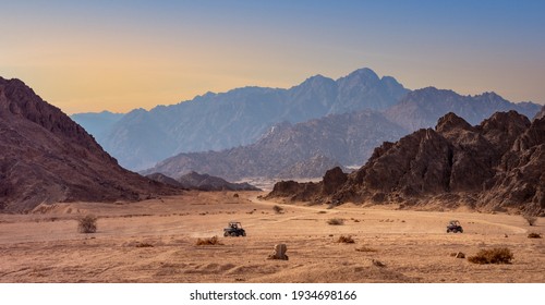 Buggy trip in a stone desert at sunset. Mountain landscape with off-road vehicles driving on a dust dirt road. Active leisure for tourists in Sharm el-Sheikh resorts, Egypt.