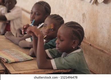 Buiba, The Gambia, Africa, May 22, 2018: Wide Angle Photography Of A Group Of Elementary School Kids In White And Green Uniforms, Sitting On Vintage Metal And Wooden Desks, Inside A Classroom